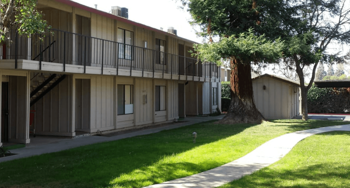 a walkway leading to an apartment building with a large tree in the background